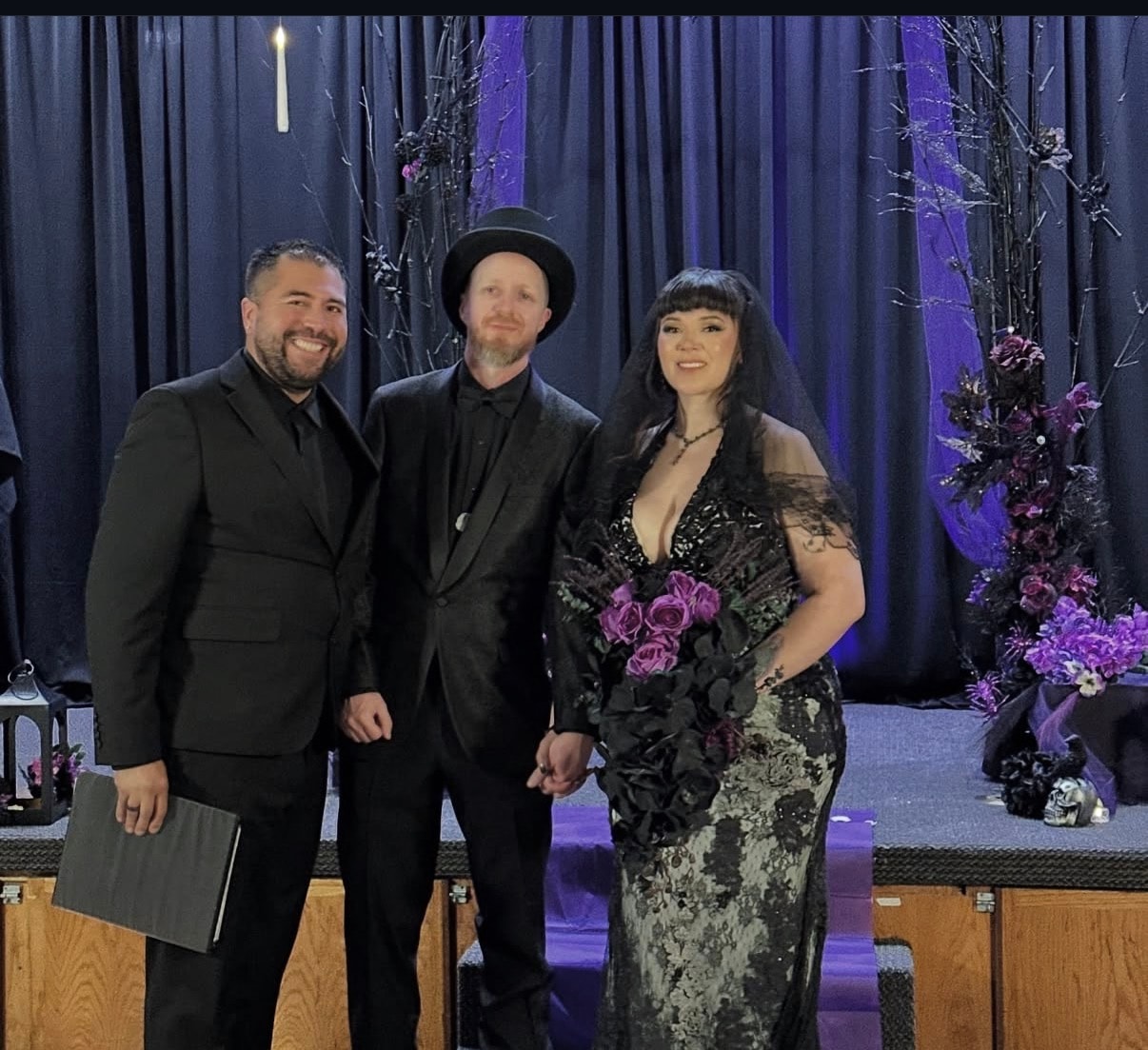 Mike with couple in gothic black dress and top hat at a purple-lit ceremony