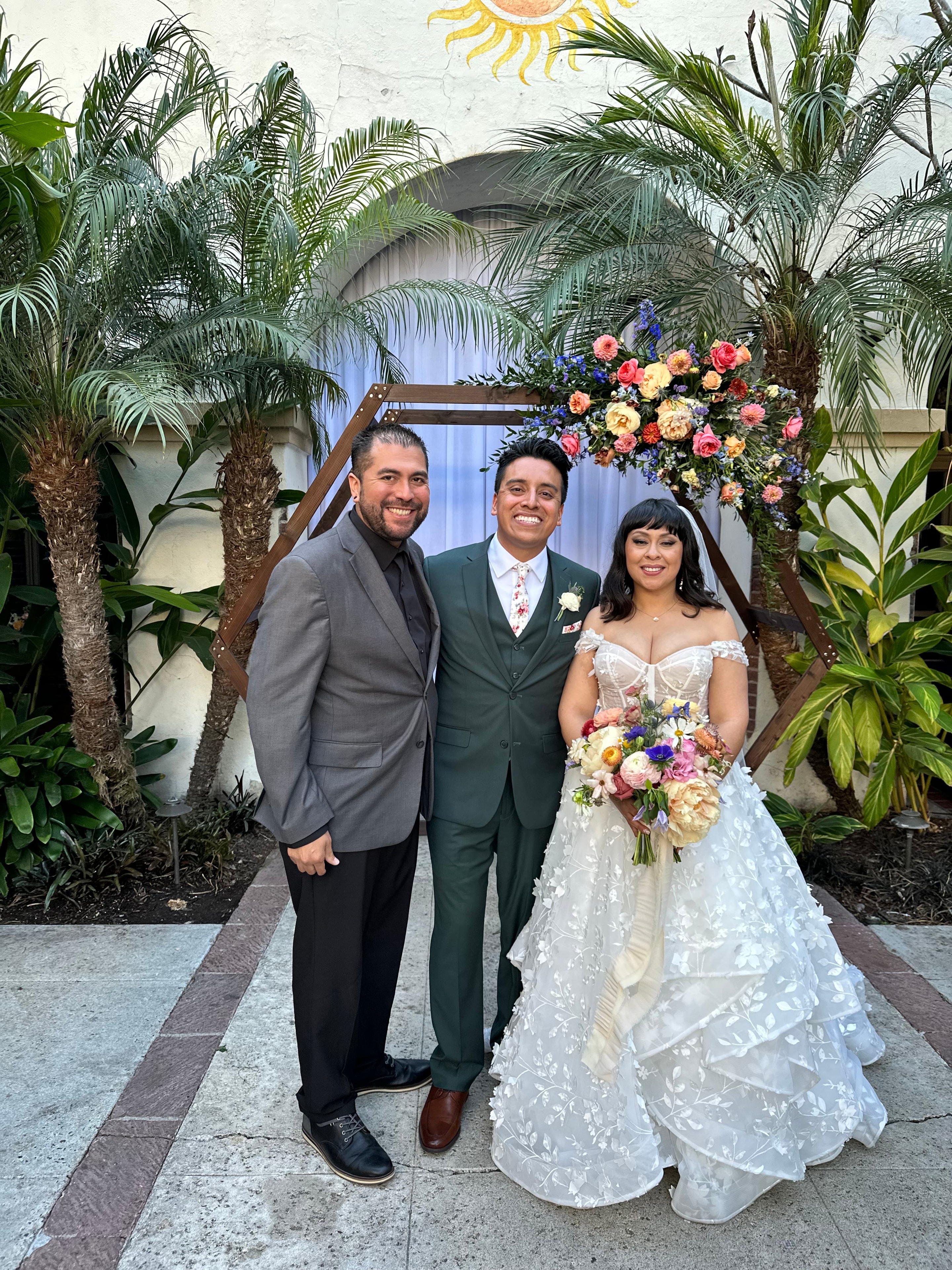 Mike with newlyweds under colorful floral arch with palm trees