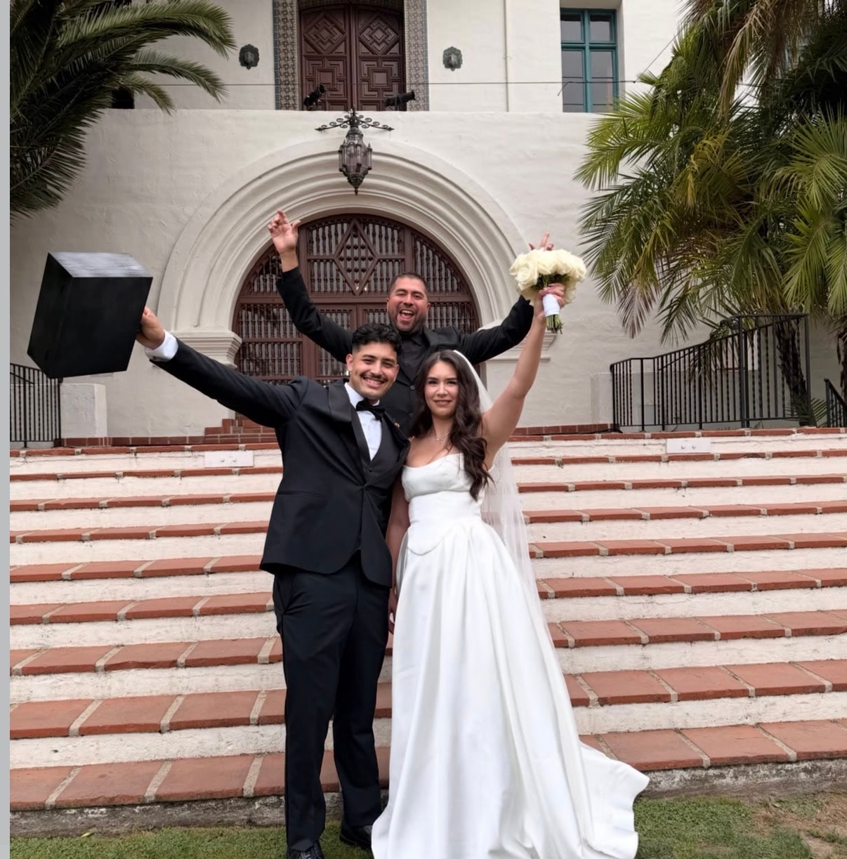 Mike and newlyweds celebrating with arms raised on courthouse steps