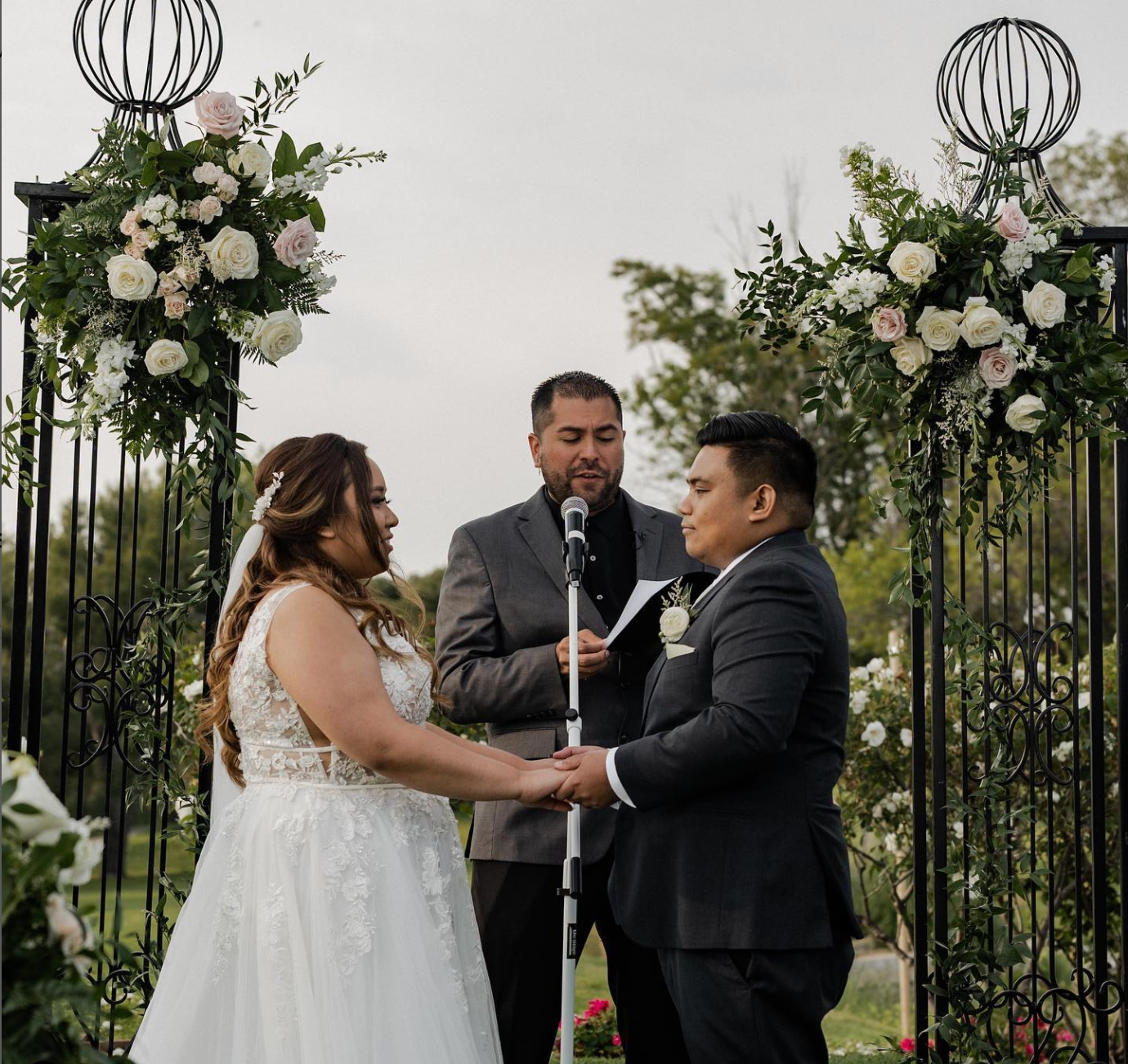 Couple sharing a joyful moment with their officiant under a white draped arch
