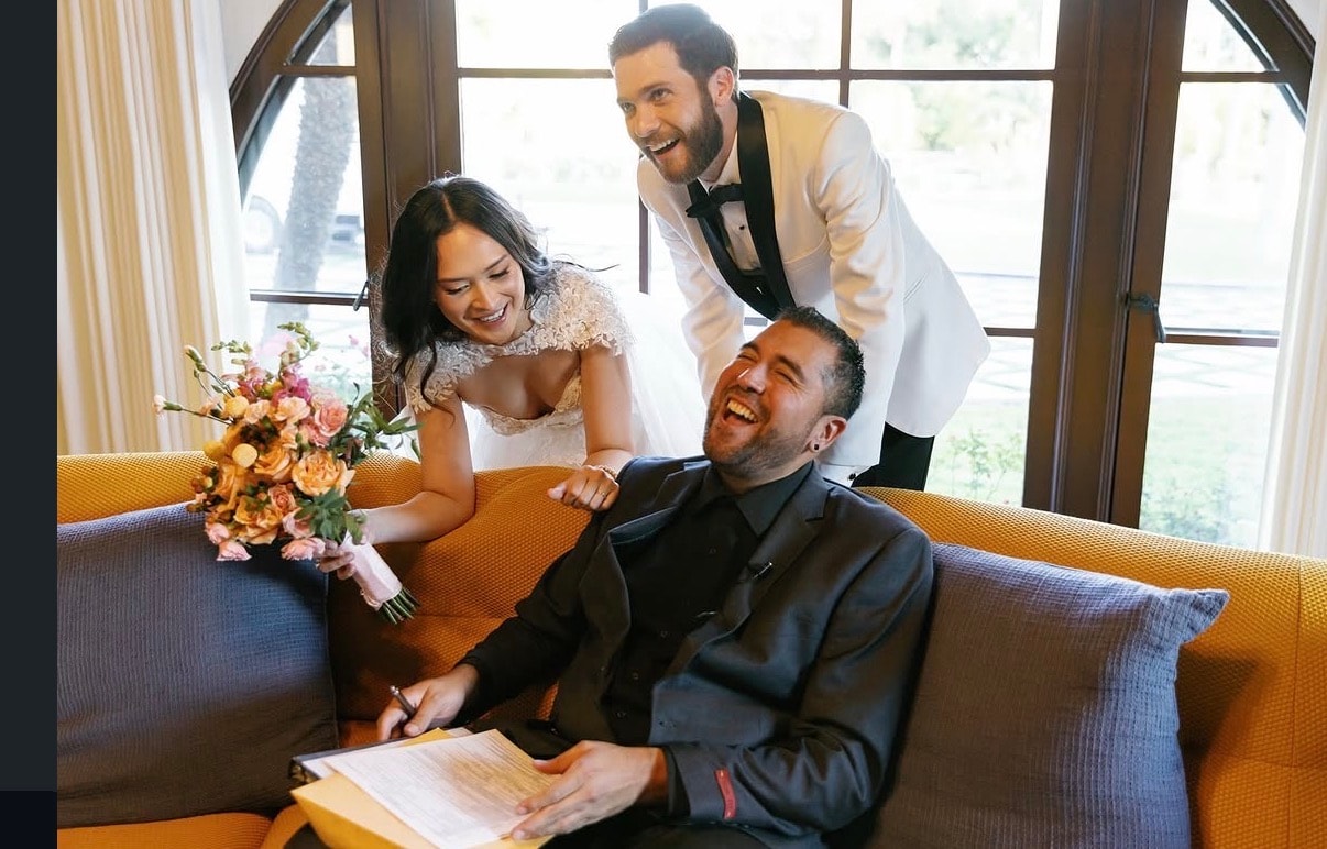 Mike laughing with a bride and groom while signing the marriage license